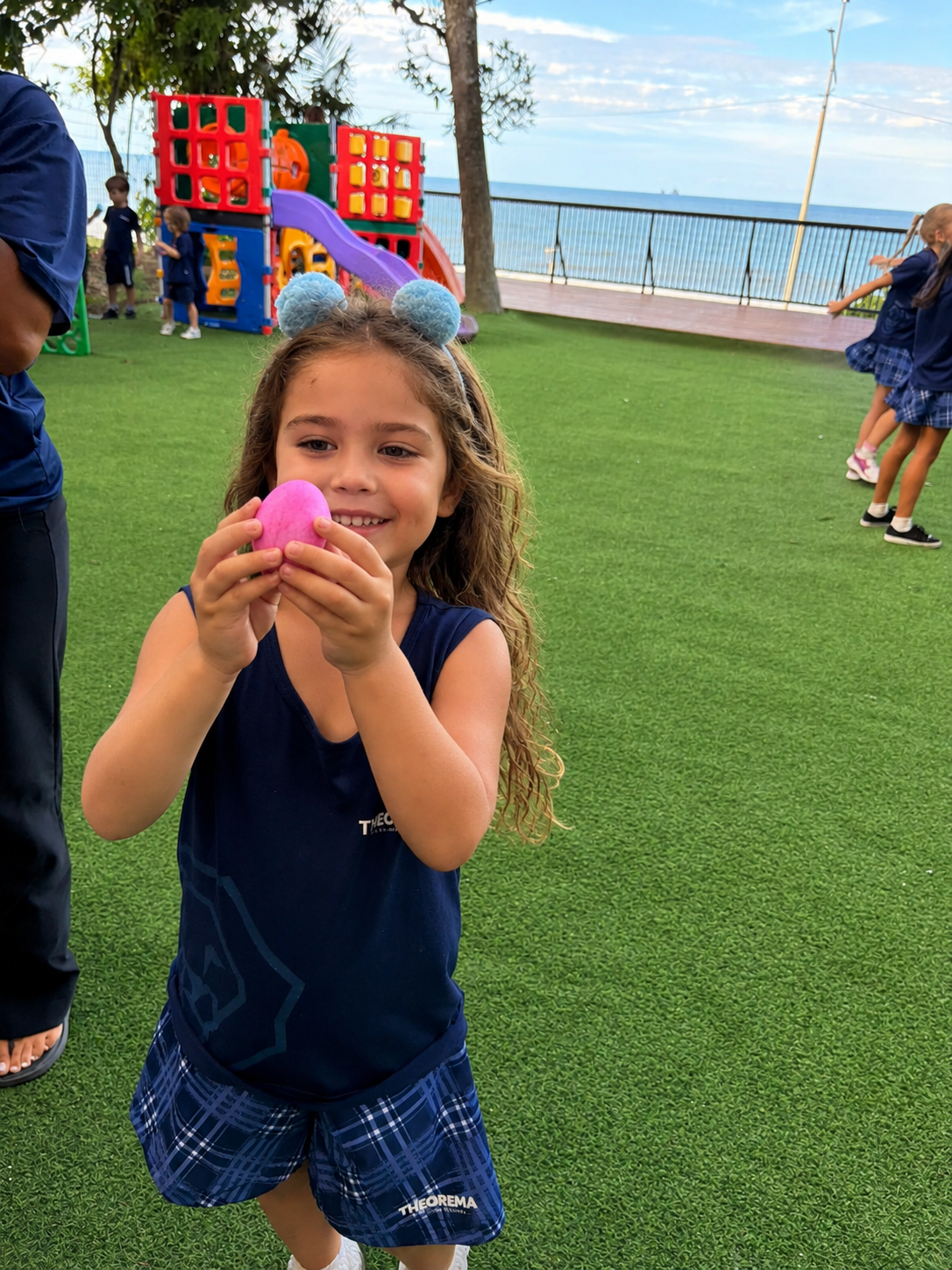 Criança sorrindo em atividade ao ar livre na Theorema Bilingual School em Balneário Piçarras, durante momento lúdico de Páscoa com aprendizagem afetiva, desenvolvimento infantil e ensino bilíngue.
